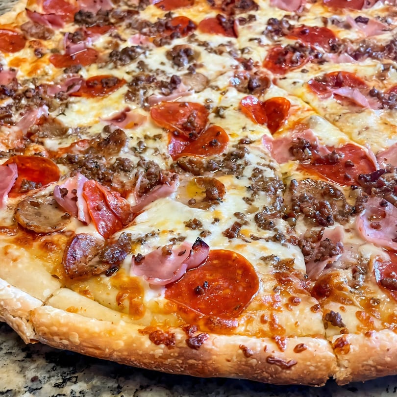 Close-up of a Di Angelo Pizza with pepperoni, ham, sausage, and melted cheese.
