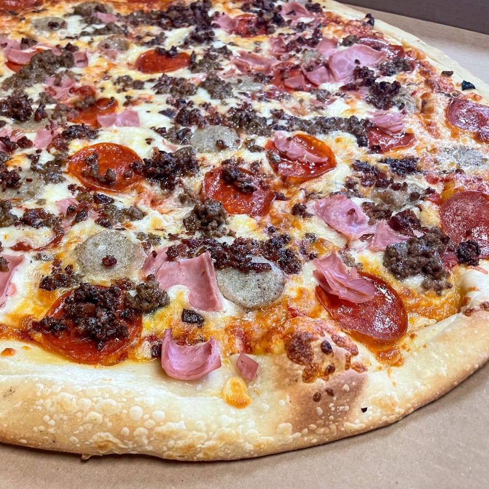 A close-up of a Di Angelo Pizza with pepperoni, sausage, ground beef, and ham toppings.