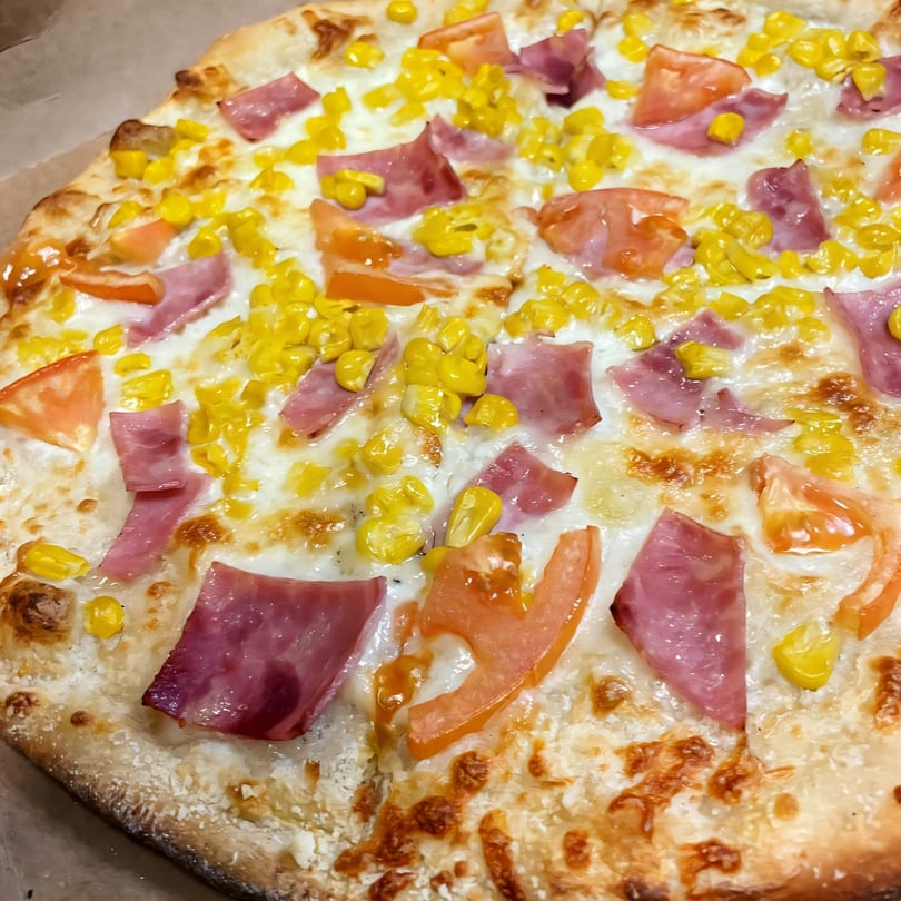 Di Angelo Pizza with ham, corn, and tomatoes on a cheesy white sauce base.